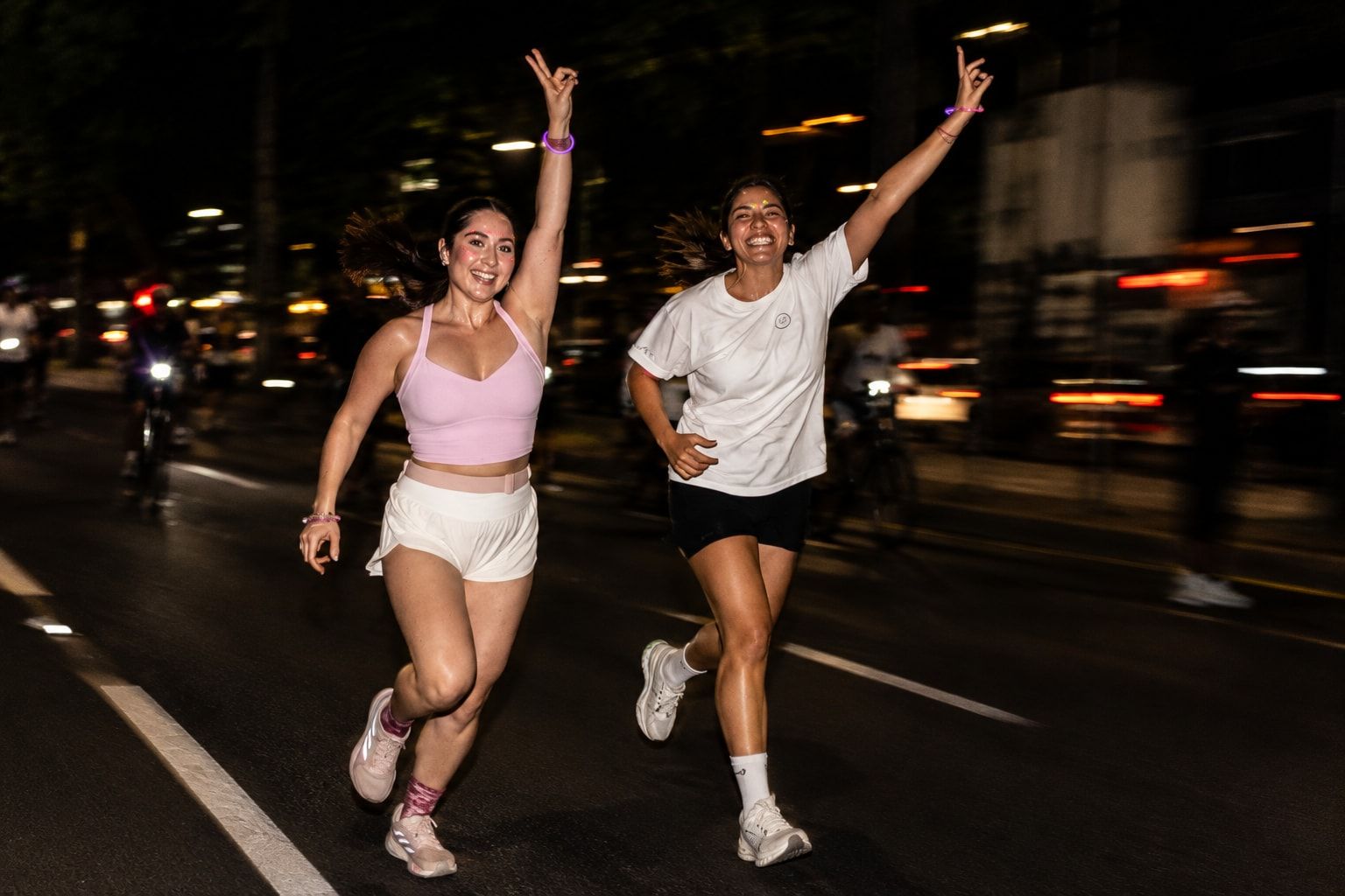 Two runners celebrating with their arms up as they run down the avenue at night