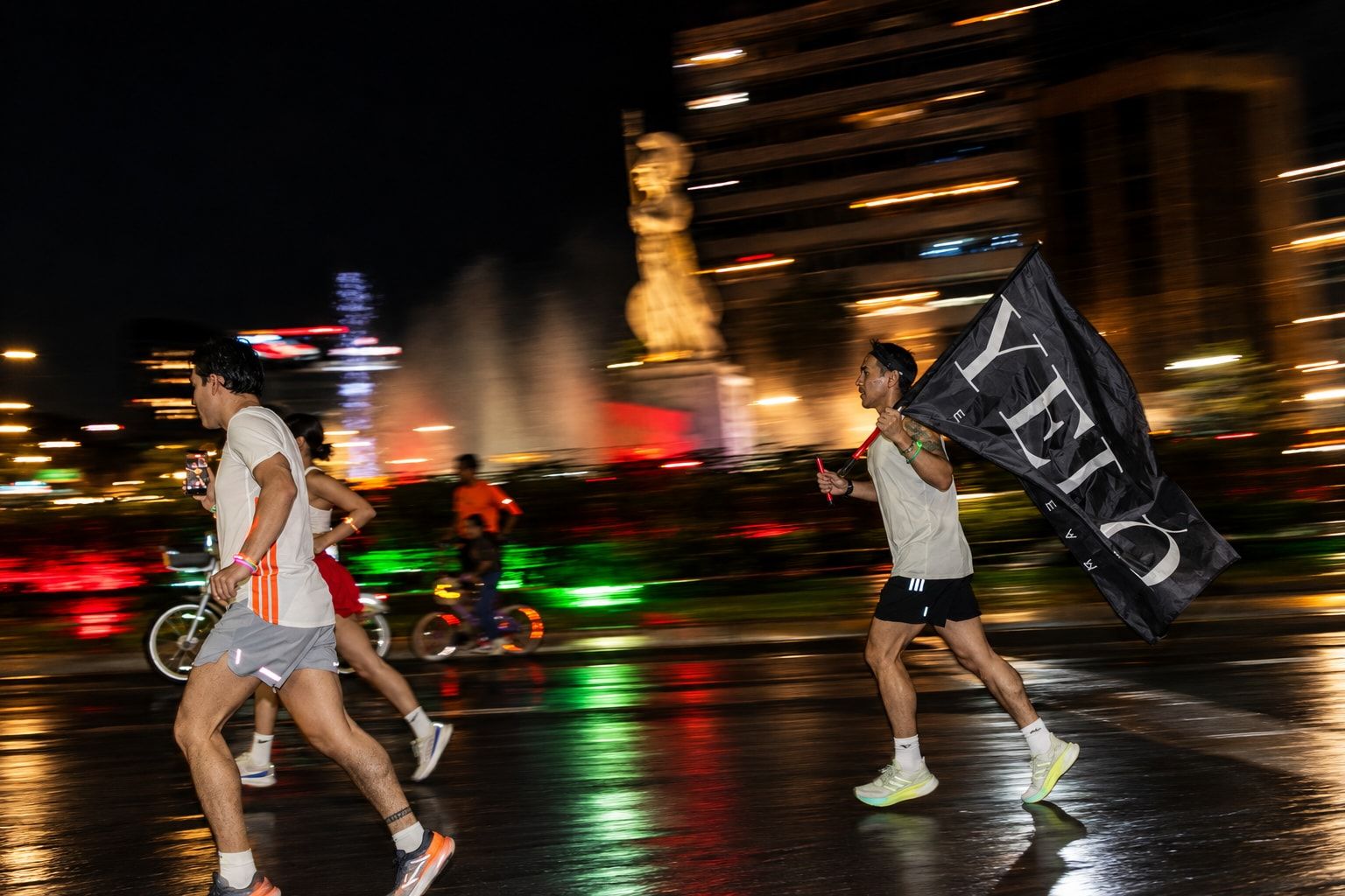 Runners carrying the Yelo flag past the illuminated La Minerva fountain