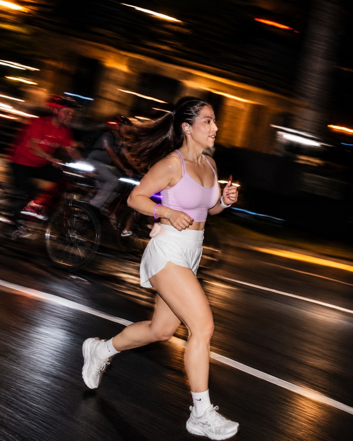 Runner mid-stride on a wet avenue with city light trails behind her
